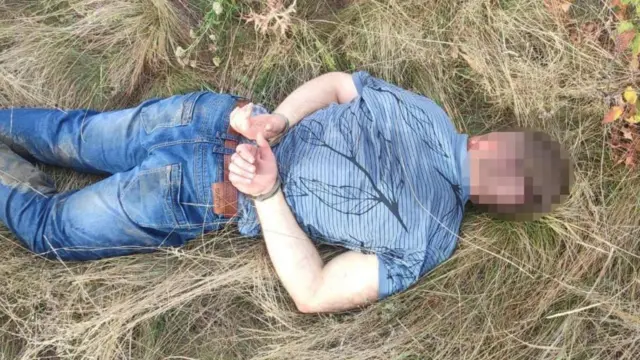 Затриманий у сорочці та джинсах лежить обличчям вниз на траві, його голова заблюрена