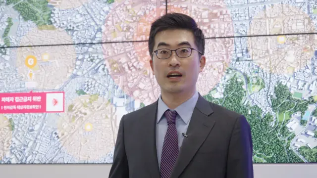 中央电子监控中心主任林合格站在一幅标示有圆形区域的大型空拍地图前。