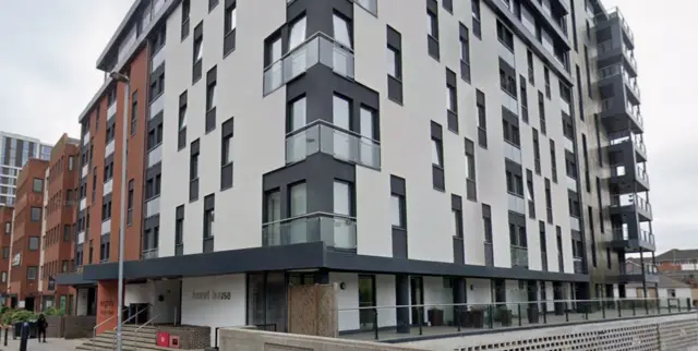 La imagen muestra el exterior de Kennet House en Reading. Es un moderno edificio de apartamentos con fachada blanca y gris.
