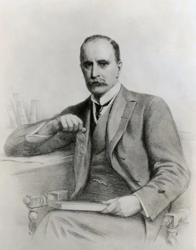 William Osler, con bigote, está sentado con un libro en una mano y en la otra tiene los lentes. Está vestido con corbata negra, chaleco y traje.
