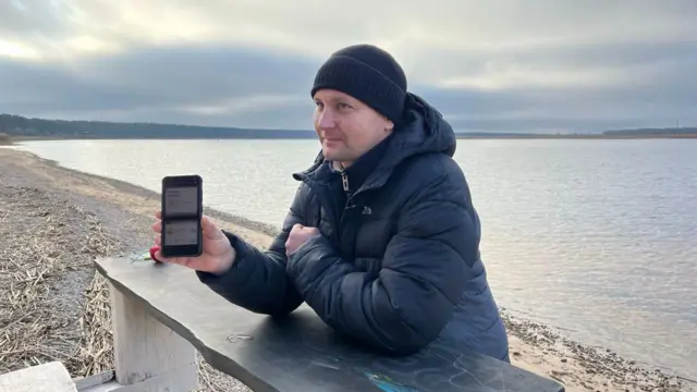 Мужчина в куртке и шапке показывает экран телефона с приложением