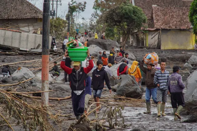 Beberapa pria membawa barang bawaan di tengah erupsi Gunung Semeru.