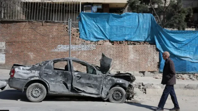 Tehranda hücumlarda yanmış avtomobilin qarşısından bir kişi keçir