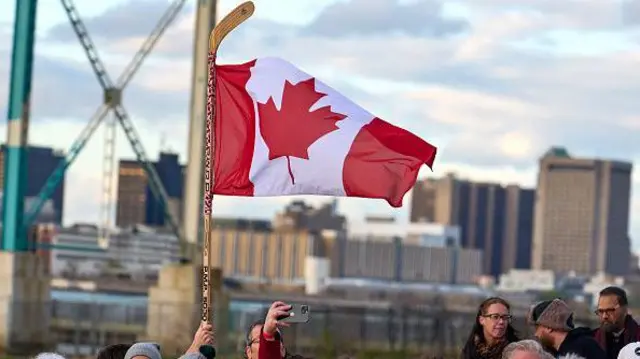 Pessoa ergue bandeira canadense presa num taco de hóquei