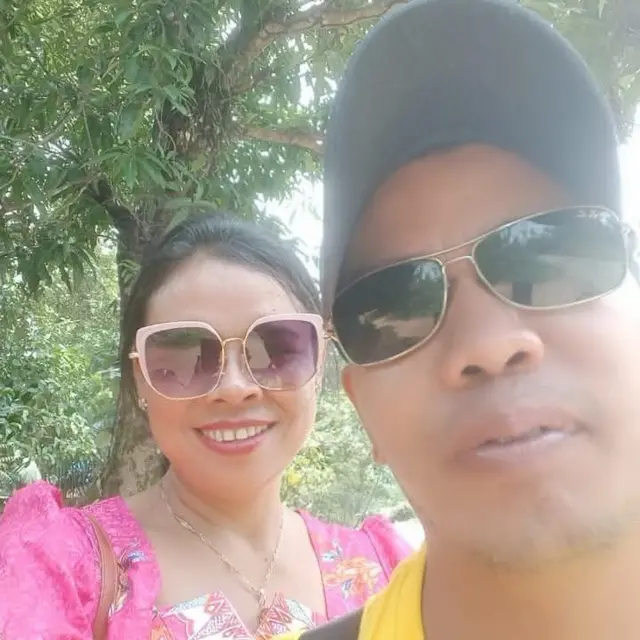 နေကာမျက်မှန်တပ်ပြီး ပန်းရောင်ပါတိတ် အင်္ကျီဝတ်ထားတဲ့ ဆရာမနဲ့ ဦးထုပ်ဆောင်း၊ နေကာမျက်မှန်တပ်ထားတဲ့ ဆရာမရဲ့ခင်ပွန်းတို့ရဲ့ selfie ပုံ 