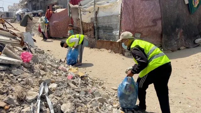 يقوم شبّان بجمع النفايات في أكياس ونقلها بعيدا عن خيام النازحين.