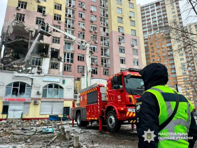 Поліцейський на тлі пошкодженого будинку 