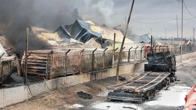 دود از کانتینرها و لاشه های سوخته در بندر شهید رجایی بندرعباس، ایران، در ۷ آوریل ۲۰۲۵، در پی یک انفجار مهیب برمی خیزد. به گفته منابع محلی، این انفجار که گمان می رود ناشی از مواد شیمیایی خطرناک باشد.