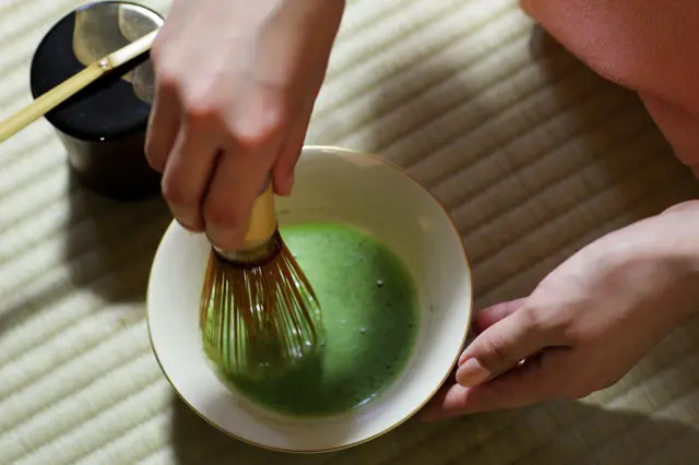 Zdjęcie przedstawiające osobę ubijającą w kubku jasnozielony, pienisty płyn.