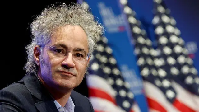 Alex Karp, com bandeiras americanas desfocadas ao fundo