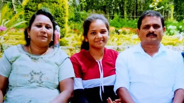 Photo de famille d'Amuthavalli, Samyuktha et Manivannan assis devant des plantes en fleurs.