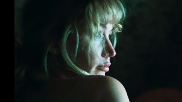 Jennifer Lawrence's face and one bare shoulder lit against a dark background in a still from Die My Love
