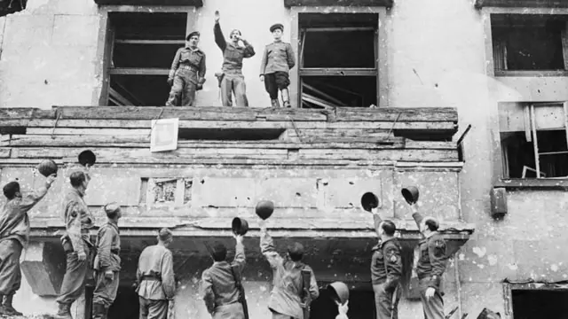 Soldados se cumprimentam na fachada de um prédio danificado pela guerra