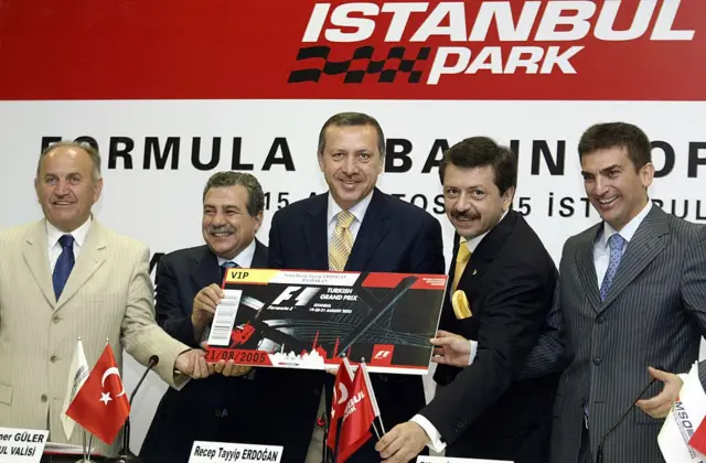 Dönemin Başbakanı Recep Tayyip Erdoğan (ortada), Türkiye Odalar ve Borsalar Birliği (TOBB) Başkanı Rifat Hisarcıklıoğlu (sağdan ikinci), İstanbul Ticaret Odası (İTO) Başkanı Murat Yalçıntaş (sağda), İstanbul Büyükşehir Belediye Başkanı Kadir Topbaş (solda) ve İstanbul Valisi Muammer Güler (soldan ikinci) ile birlikte, İstanbul Park'taki ilk F1 Türkiye Grand Prix’sinden birkaç gün önce, 15 Ağustos 2005’te düzenlenen basın toplantısında büyütülmüş bir F1 bileti takdim ediliyor.