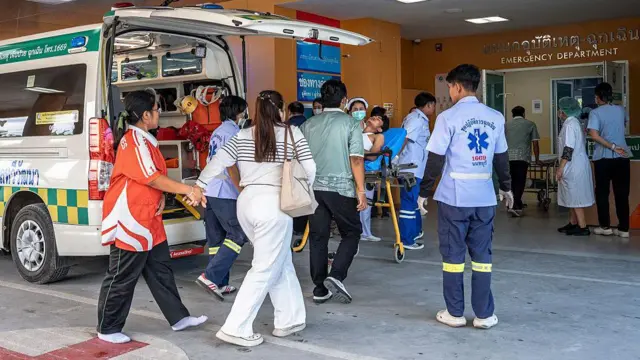 Mai mulți oameni se află în fața intrării într-un spital, în timp ce o victimă este transportată pe o targă.