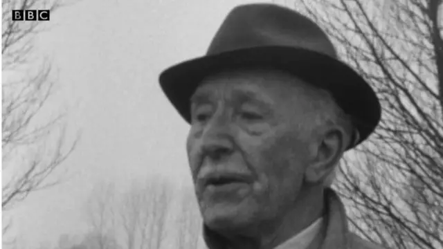 Скрін із відео, чорно-біле фото чоловіка у віці з вусами та в капелюсі на фоні неба та гілок дерев