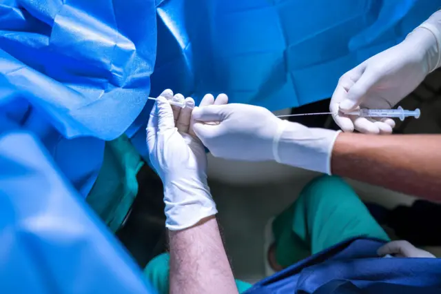 Лікар проводить процедуру ембіро трансферу пацієнтці, вкритій синьою тканиною 