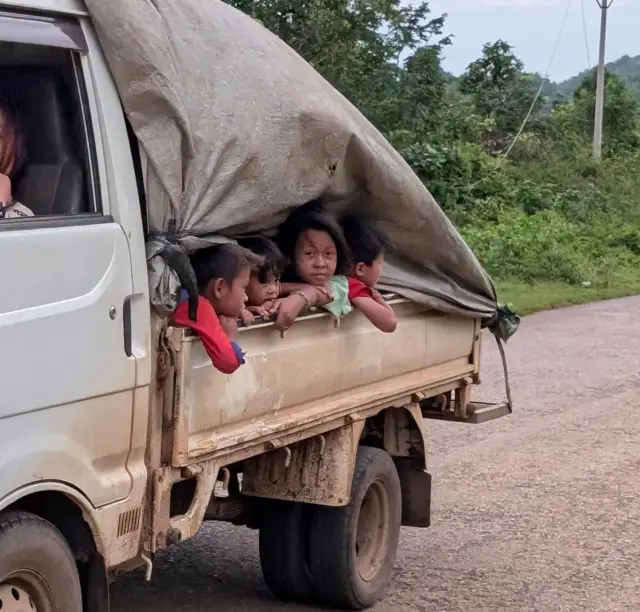 မိုးကာအမဲအုပ်ထားတဲ့ အမိုးဖွင့် ထရပ်ကားအနောက်မှာ လိုက်လာတဲ့ ကလေး ၄ ဦး