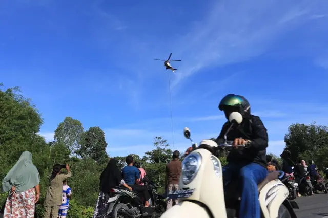 Warga melintas di bawah helikopter yang memadamkan api di Aceh Barat.