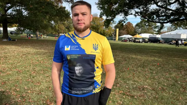 Dmytro Kamenschyk com camiseta azul e amarela, cores da bandeira da Ucrânia, e a foto do pai deleapk bet365 2024preto e branco