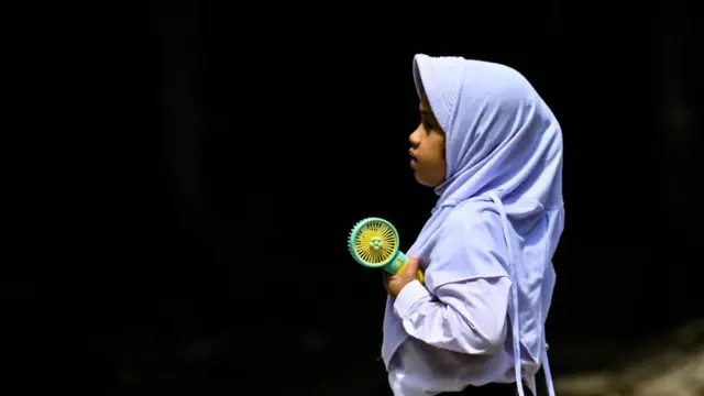 Uma menina tentando se refrescar com um ventiladorpoker supremamãopoker supremameio a uma ondapoker supremacalor na Indonésia este ano