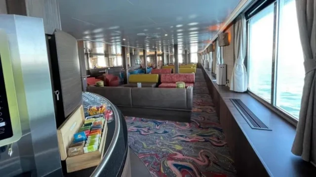 Общее помещение на судне MV Hondius. Ряды диванов, широкие окна, на переднем плане место, где можно налить себе чай, и коробка с чайными пакетиками.