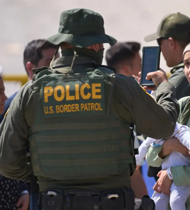 Um agente da Patrulha de Fronteira dos EUA tirando uma foto de uma imigrante com um celular