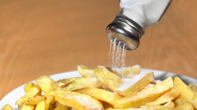 La sal cae de un salero hacia las papas fritas.