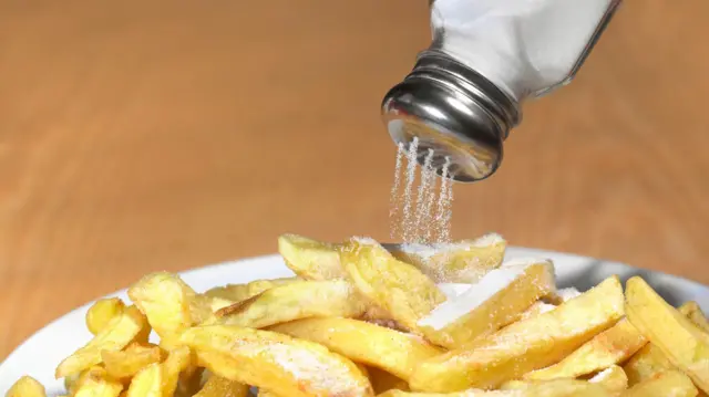 La sal cae de un salero hacia las papas fritas.