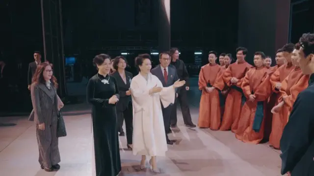 北京中国国家大剧院内彭丽媛（中，白衣者）向吴芳璃（左二，身穿黑色奥黛）介绍某演出项目的表演者（中国中央电视台片段截屏 15/4/2026）