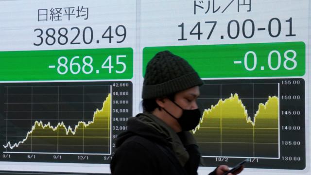 Uma pessoa caminha na frente de gráficos econômicos