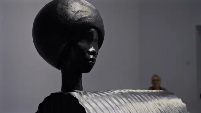 Une sculpture noire représentant la tête d'une femme d'origine africaine fixée à un tunnel en fer.