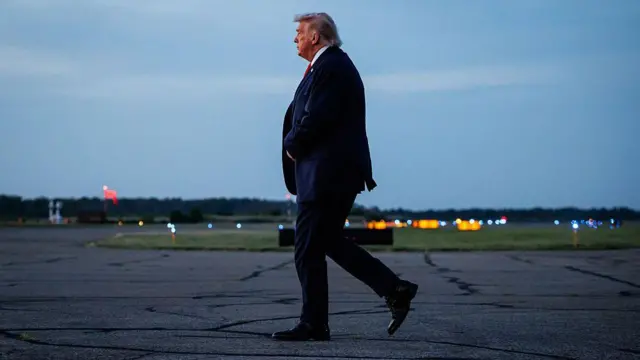 Donald Trump, visto de perfil, caminhando sozinho na pista de um aeroporto.