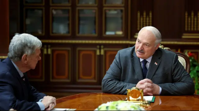 Переговоры между Александром Лукашенко (в сером костюме и синем галстуке) и Джо Коулом (в синем костюме; сидит в половину оборота к Лукашенко) в Минске. Собеседники сидят рядом за овальным столом, коричневого лакового цвета, на заднем плане - стеллажи такой же расцветки