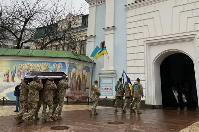 Военные вносят гроб в собор, впереди идут военные с флагом