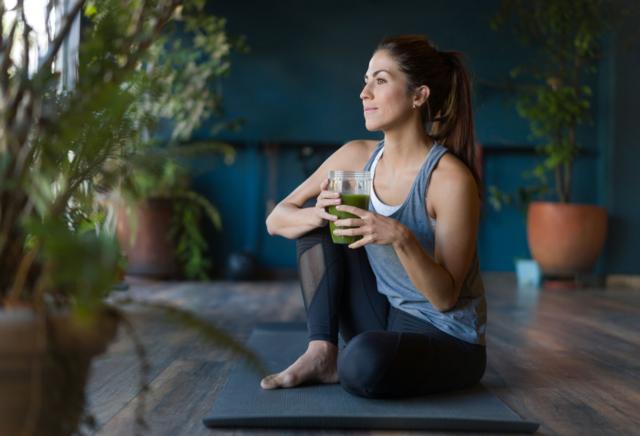 Una mujer joven toma un jugo verde antes de comenzar su clase de yoga