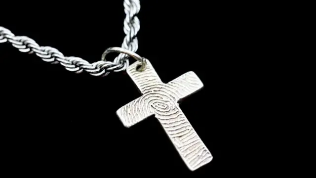 Cruz de prata presa a uma corrente prateada sobre fundo preto