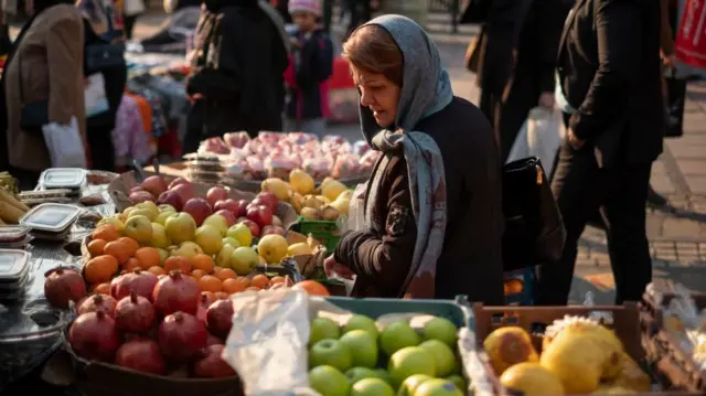 یک زن ایرانی در حال خرید از یک فروشنده در مرکز شهر تهران است