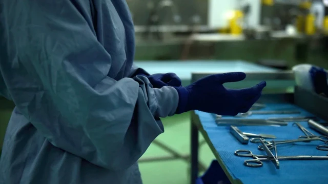 جراحی در حال پوشیدن دستکش در برابر میز با وسایل جراحی