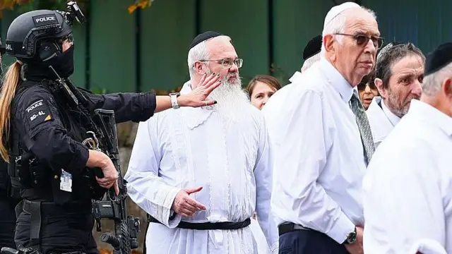 Rabbi Daniel Walker, wọ aṣọ funfun dúró láàárín àwọn ọlọ́pàá ní ìta synagogue