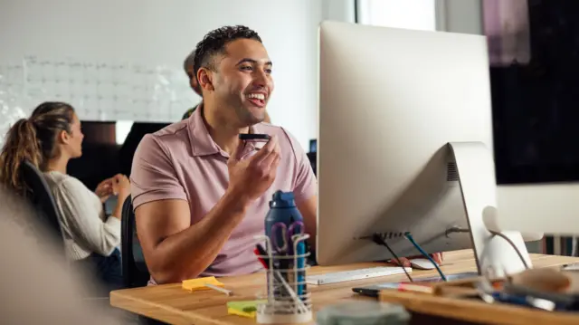 Funcionário sorrindoretirada sportingbetfrente ao computador no escritório