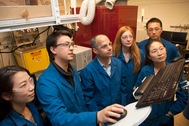 Yaghi con una bata azul rodeado de estudiantes también con batas azules