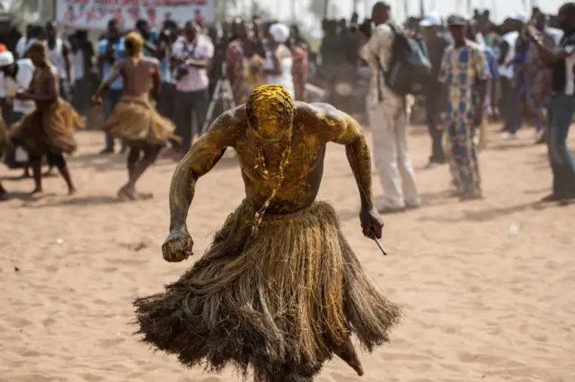 Un adepte de vodoun qui a aspergé son corps avec de la poudre et de l'huile rouge, porte une tenue traditionnelle et danse dans une arène.
