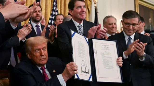 ترامپ نشسته و قانونی را که امضاء کرده به سمت حضار و دوربینها نگه داشته، دیگران ایستادهاند و کف میزنند