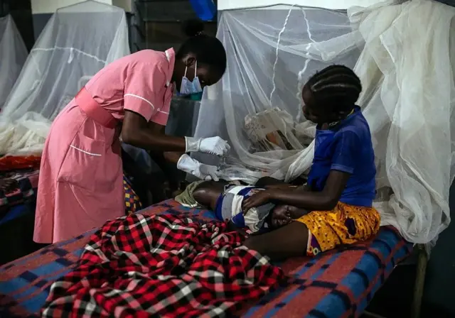 Une infirmière effectue des soins sur une patiente assise sur un lit d'hopital. 