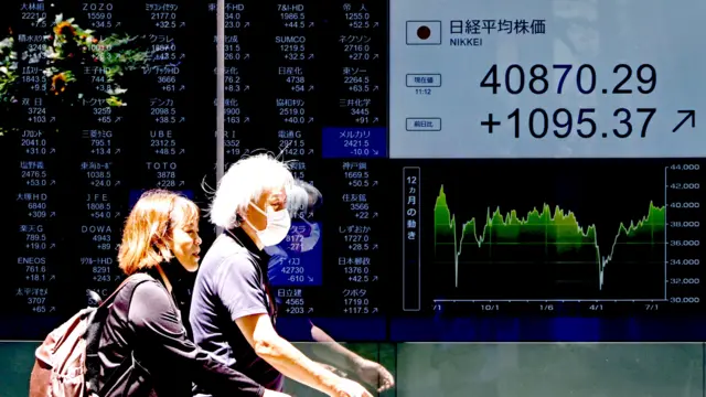 东京某金融机构外行人走过股市报价屏幕（23/7/2025）
