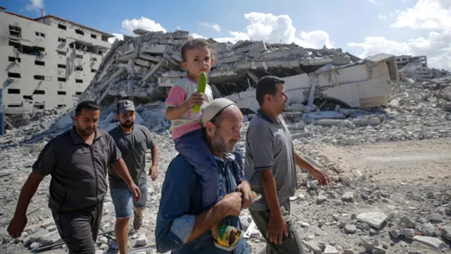 Varios hombres, uno de ellos con un niño a hombros, caminan entre los escombros en la Franja de Gaza en octubre de 2025