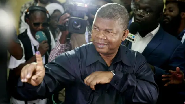 Joao Lourenco yerekana urutoke ruriko irangi ahejeje gutora. Akikujwe n'abamenyeshamakuru kandi yambaye ishati yirabura yuguruye mw'izosi. 