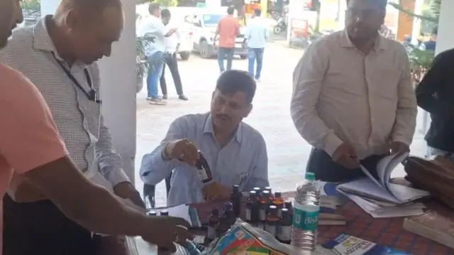 सरकारी अधिकारी ज़ब्त की गई कफ़ सिरप को देखते हुए