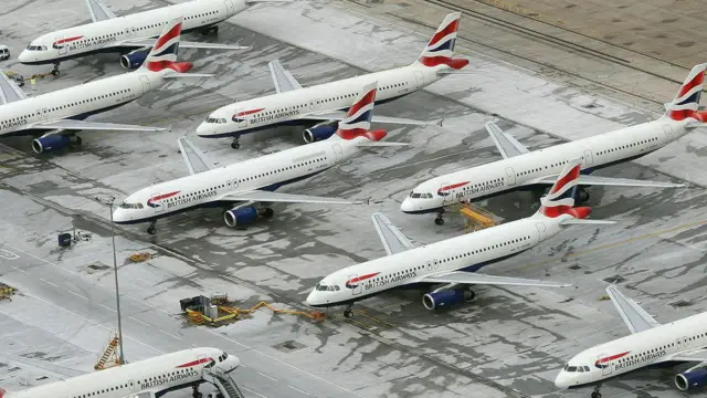 Vista aérea de um grupo de aviões da British Airways estacionados em fileiras, com as aeronaves próximas entre si e equipamentos de serviço ao redor 